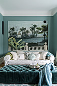Pale sofa with scatter cushions below large art print and ottoman in foreground in green interior