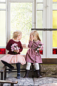 Zwei Mädchen mit Blumen am Altbaufenster mit Buntglas