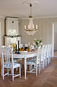 Corner tiled stove and large white dining table with wooden chairs in dining room of manor house