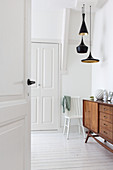 Open panelled door leading into white hallway with white wooden floor and wooden sideboard
