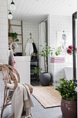 White-tiled, Bohemian-style bathroom with houseplants and wicker chair