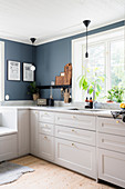 Weiße Küchenzeile mit Marmor-Arbeitsplatte vor Fenster in Küche mit grau-blauer Wand