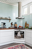 Cooker with modern, stainless steel extractor hood in corner of kitchen with pale blue wall tiles