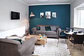 Living room with grey sofa set, dining table and chairs and petrol-blue wall