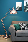 Grey sofa and standard lamp in living room with petrol-blue wall
