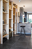 Floor-to-ceiling wooden shelves and breakfast bar in open-plan living space with tiled floor