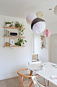 Lanterns and honeycomb balls above dining table and next to wall-mounted shelves