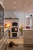 Weihnachtlich dekorierte weiße Küche mit Holzofen, Hund auf dem Boden