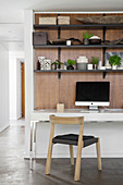 Desk and shelves on wooden wall panel in open-plan interior