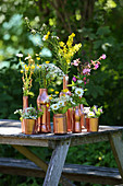 Wildflowers in copper-coloured containers on wooden table in garden
