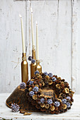 Bottles sprayed gold and used as candlesticks behind handmade wreath of pine cones