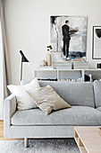 Grey sofa in front of half-height shelves, stacked magazines and painting