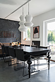 Modern, white pendant lamps above black dining table with turned wooden legs
