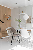 Dining table and various Eames chairs in white interior with wooden elements