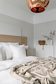 Double bed with slatted wooden headboard below copper-coloured spherical lamp