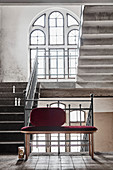 Bench with claret-red upholstery in stairwell with arched window
