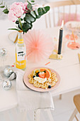 Waffel mit Früchten auf festlich dekoriertem Tisch mit Glitzerkugeln, Kerze und Papierrosette
