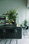 Charcoal-grey island counter with bar stools and lemon tree planted in centre in kitchen of loft apartment