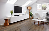 Wohnzimmer mit Lowboard, Fernseher an der Wand, Stehleuchte, Sofa und Coffeetable im Dachzimmer