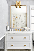 Bathroom washstand with marble top and brass fittings below mirror and wall lamps