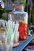 Glasses, straws and punch in glass dispenser on garden table