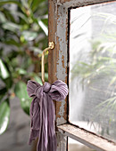 Schleife aus lilafarbenem Tuch am Türgriff einer alten Sprossentür