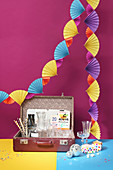 Colourful garland of paper fans above open suitcase used as drinks tray