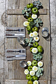 Girlande aus weißen Pompondahlien, grünen Tomaten und Hauswurz auf rustikalem Tisch