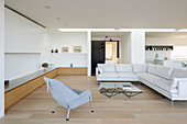 Pale sofa set, coffee table, armchair and low, custom sideboard in open-plan interior