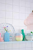 Crockery and ornaments in pastel shades on kitchen shelf on white tiled wall
