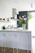 Vase of colourful flower on counter with bar stools in kitchen