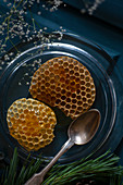 Honeycomb oozing honey on glass plate with silver spoon