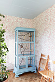 Pale blue aviary made from old cupboard against floral wallpaper
