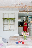 Esszimmer mit Wassermelone und Sommerstrauß, im Hintergrund Frau in offener Küche