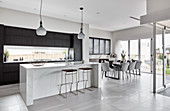 Kitchen counter with bar stools and dining area in open-plan interior with tiled floor