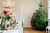 Long, festively set dining table and Christmas tree in dining room of manor house