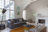 Grey sofa, classic standard lamp and coffee table in front of fireplace in white-painted log cabin