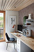 Desk with pale wooden top below shelves on patterned wallpaper