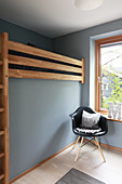 Loft bed and classic chair next to window in pale grey child's bedroom