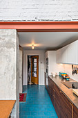 Elongated kitchen with bright blue floor tiles and concrete walls