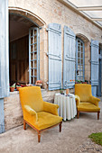 Zwei Ockergelbe Sessel auf überdachter Terrasse eines mediterranen Landhauses