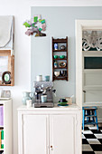 Espresso machine on white cabinet below small, wall-mounted shelving unit