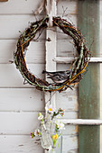 Wreath made of branches with bird ornament and flowers in small bottle