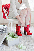 Woman sitting on white chair putting on red boots