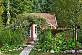 Garden beds and climbing arch in front of a Swedish cottage