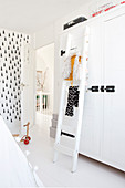 White ladder in front of white wardrobe in child's bedroom with black-and-white wallpaper