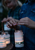 Children's hands hold homemade jar lantern