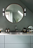 A round mirror above a washbasin