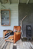 An old leather chair next to a wood-burning stove and a wall cupboard in a glass house