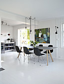 A dining table with black classic chairs and a pendant light above in an open-plan living area